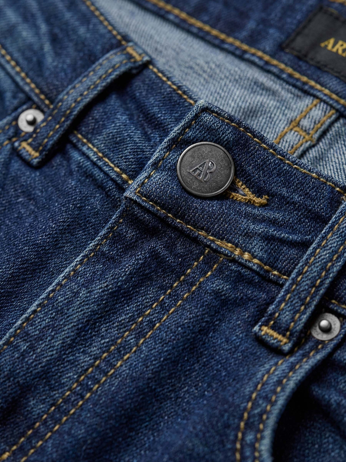 Close-up of blue jeans waistband with branded button and reinforced stitching