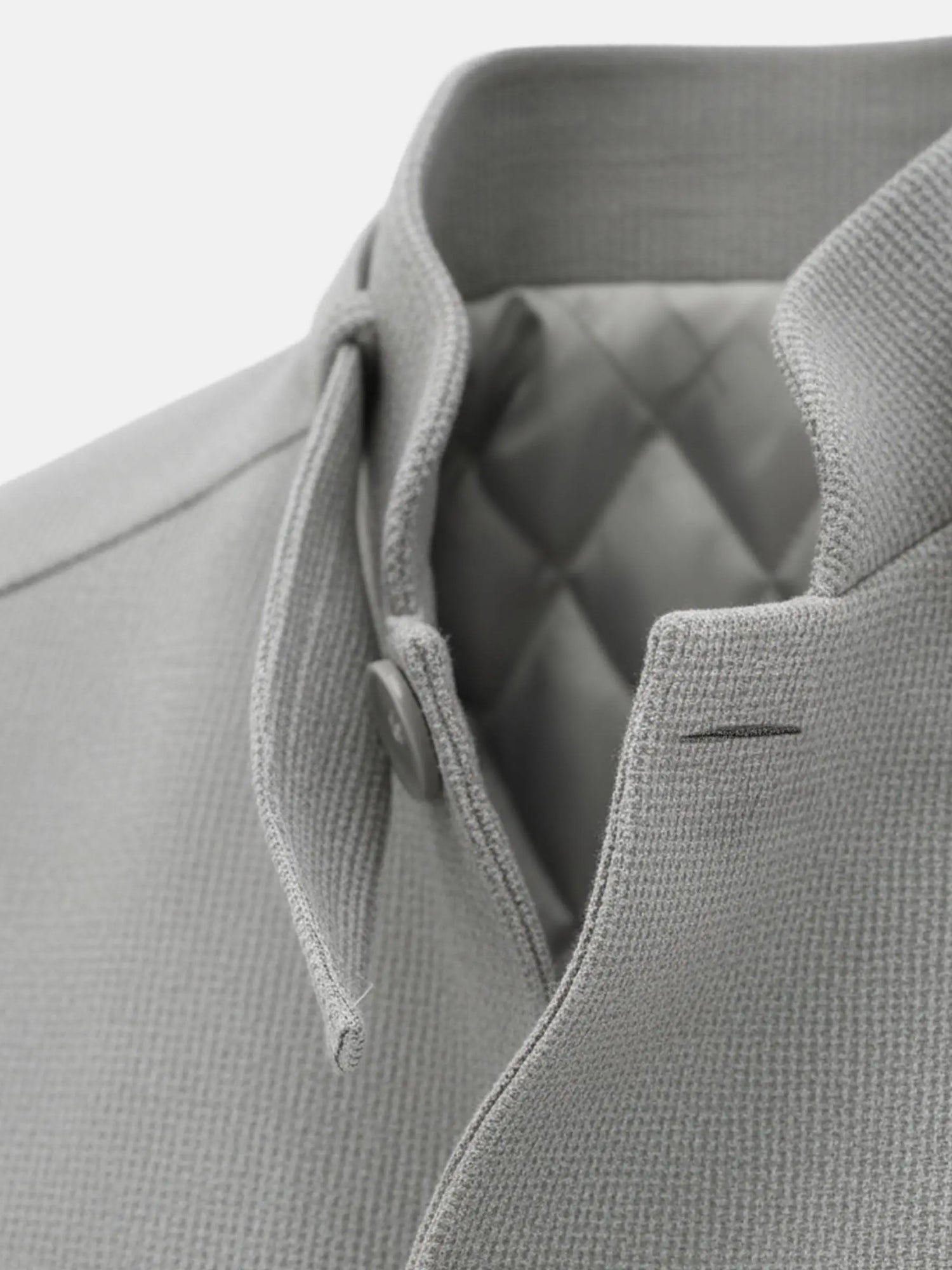 Close-up of grey trenchcoat collar with textured fabric and quilted inner lining.